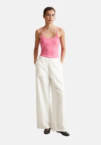 Rosa geripptes Tanktop, weiße weit geschnittene Hose, schwarze flache Schuhe. Glatte Textur, enganliegendes Oberteil, elastischer Bund und lockere Passform bei der Hose.