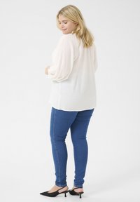 Luźna biała bluzka z teksturowanej tkaniny, z pełnymi rękawami, zestawiona z niebieskimi skinny jeansami i czarnymi szpilkami z migdałowym noskiem. Prosty i casualowy zestaw.