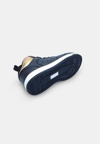Sportlicher Schuh in Marineblau mit Steppmuster, goldenen Akzenten, einer weißen Mittelsohle und einer strukturierten schwarzen Gummisohle mit Grip-Mustern.