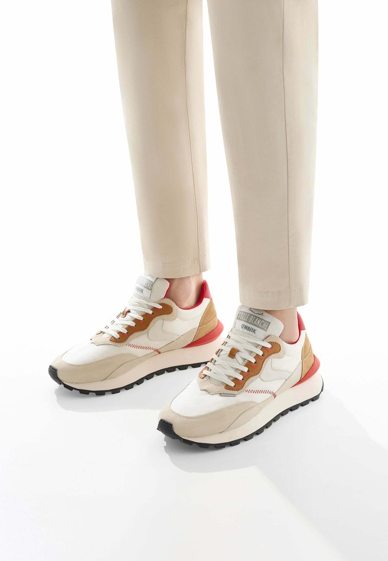 Sneaker con tomaia in mesh bianco, dettagli in suede beige, tallone rosso e lacci marroni. Suola intermedia spessa bianca con battistrada in gomma nera.