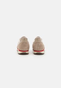 Zapatillas de ante beiges con acentos rojos, con suela acolchada y diseño minimalista. Punta redonda y cuello acolchado para mayor comodidad.