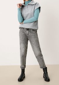 Grå stickad tröja med hög krage, lagd över en turkos långärmad topp. Matchas med urblekta gråjeans och svarta ankelstövlar.