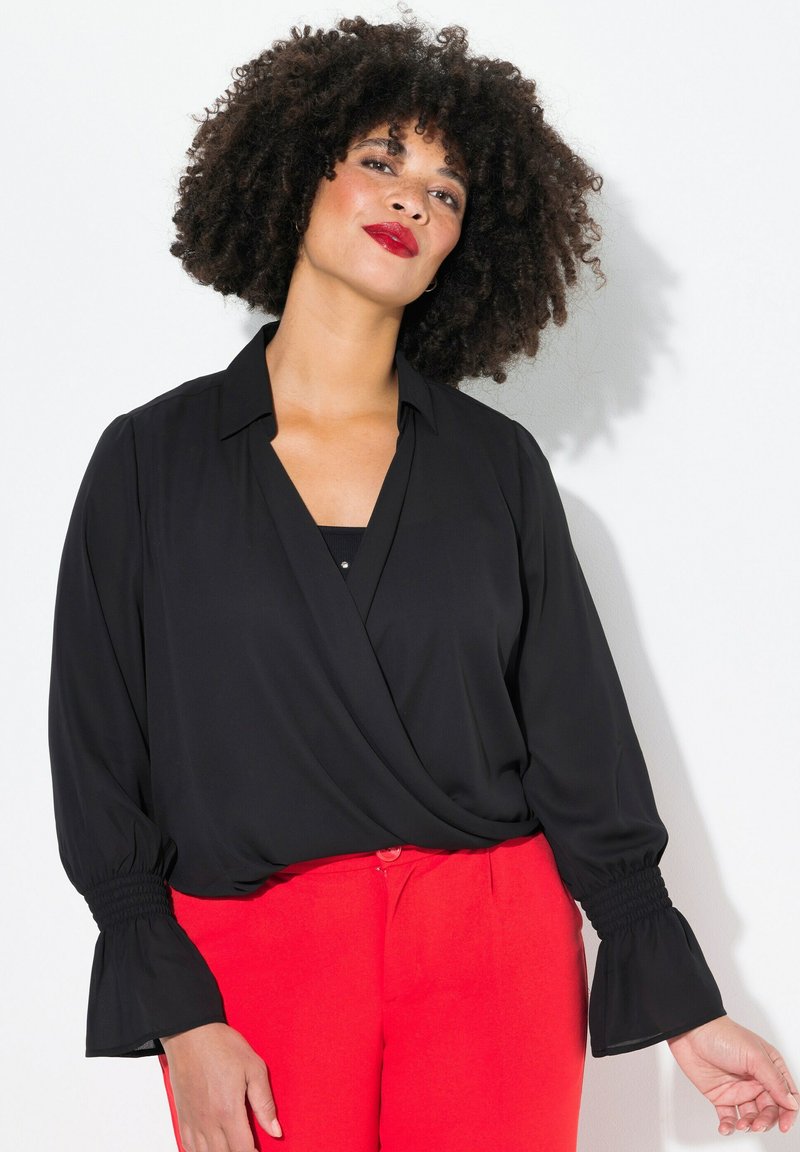 Schwarze Wickelbluse mit Kragen und langen, gerafften Ärmeln. Kombiniert mit leuchtend roten Hosen, die eine glatte Stofftextur zeigen.