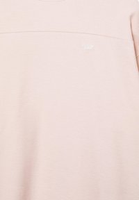 Sweat-shirt rose clair avec tissu subtilement texturé et petit logo blanc « Swiz » sur la partie supérieure de la poitrine.