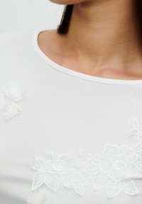 Hvid skjorte med blomsterbroderi i et struktureret design, rund halsudskæring og subtile hævede detaljer på stoffet.
