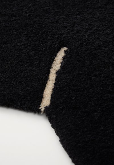 Zwart gestructureerde stof met een uitsnijding die een beige achterkant blootlegt. Het oppervlak is fuzzy, wat de zachte textuur en de contrasterende kleuren benadrukt.