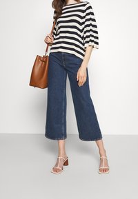 Pasiasty czarno-biały top, szerokie niebieskie dżinsowe kuloty i beżowe sandały na obcasie z paskami. Brązowa torba na ramię z paskiem na ramię.