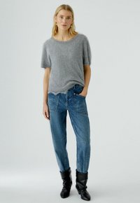 Grijze fuzzy korte mouwen trui gecombineerd met hoge taille blauwe jeans met patchzakken, voornaden en zwarte kniehoge laarzen.