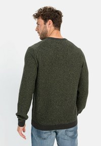 Knit sweater in dark green with textured pattern, ribbed cuffs and hem. Styled with casual blue jeans, shown from the back.