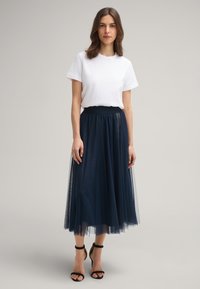 T-shirt blanc en coton associé à une jupe midi en tulle marine avec une taille élastique noire. Des talons à lanières noirs complètent la tenue.