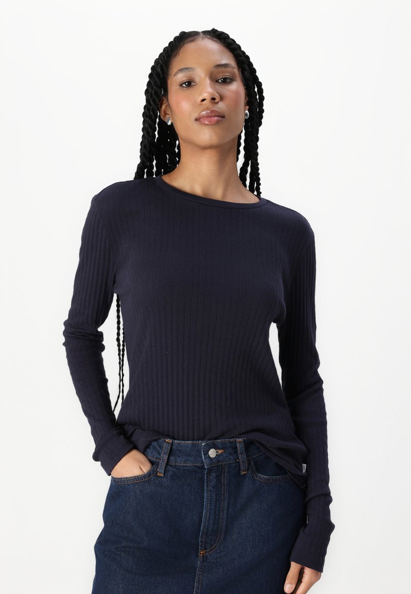 Dunkelblaues, geripptes Langarmoberteil mit rundem Ausschnitt, kombiniert mit einem hochtaillierten Denimrock, der locker sitzt und eine strukturierte Oberfläche bietet.