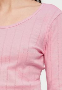 Ροζ ριμπ πλεκτό μακρυμάνικο τοπ με στρογγυλή λαιμόκοψη. Το ύφασμα έχει κάθετες ρίγες και μικρές τρυπητές λεπτομέρειες για υφή.