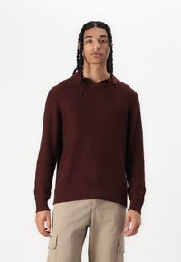 Pull en tricot bordeaux avec capuche, texture côtelée, manches longues et coupe décontractée. Associé à un pantalon cargo beige avec poches latérales.