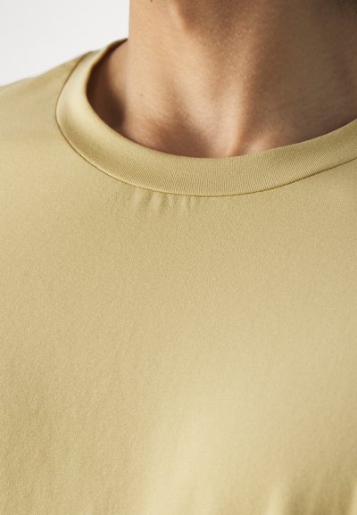 Camiseta de algodón amarilla con cuello redondo y una textura suave y lisa. La tela es elástica y tiene un sutil detalle acanalado alrededor del cuello.