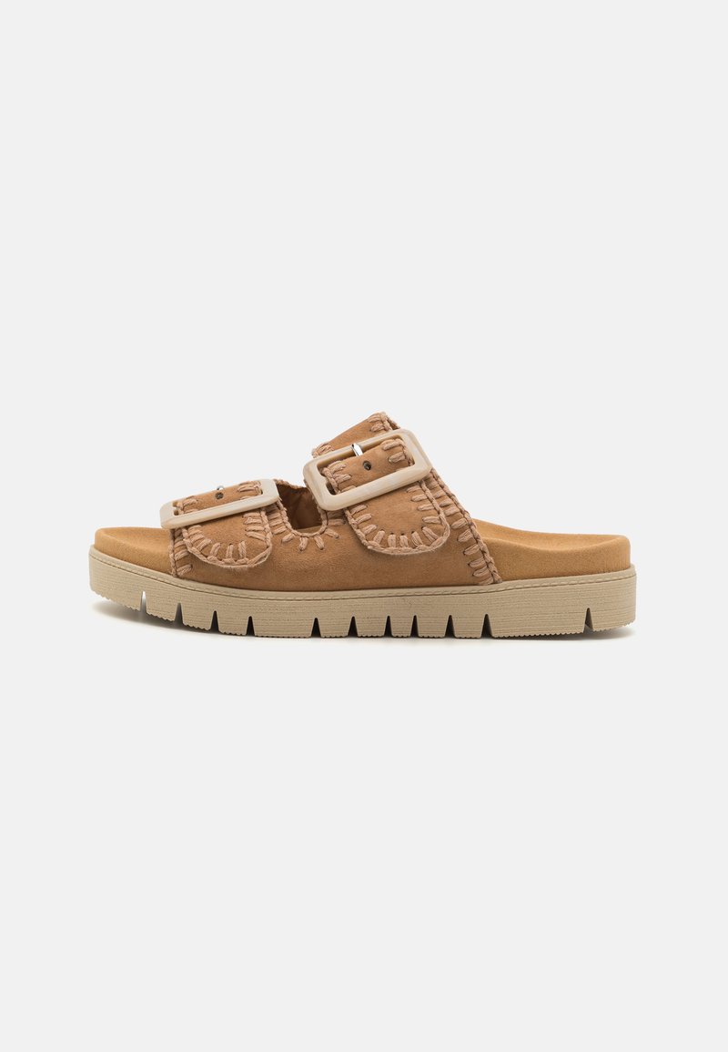 Sandales en suédine beige avec deux boucles réglables, des détails de couture texturés, et une semelle en caoutchouc beige épaisse avec un bord cranté.