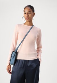 Top a maniche lunghe a coste rosa chiaro con scollo rotondo, abbinato a pantaloni in satin blu scuro e una borsa a tracolla blu.