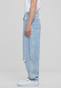 Jeans de mezclilla azul claro con un corte relajado, que presentan un detalle desgastado cerca del tobillo y un diseño de cintura alta. Se llevan con zapatillas blancas.