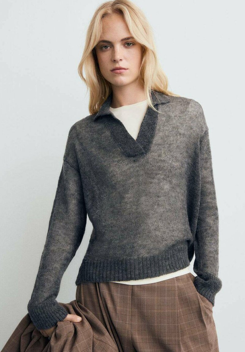 Pull en maille texturée gris avec un col en V et un col, doté de manches longues et d'un ourlet côtelé. Associé à un pantalon à carreaux marron.