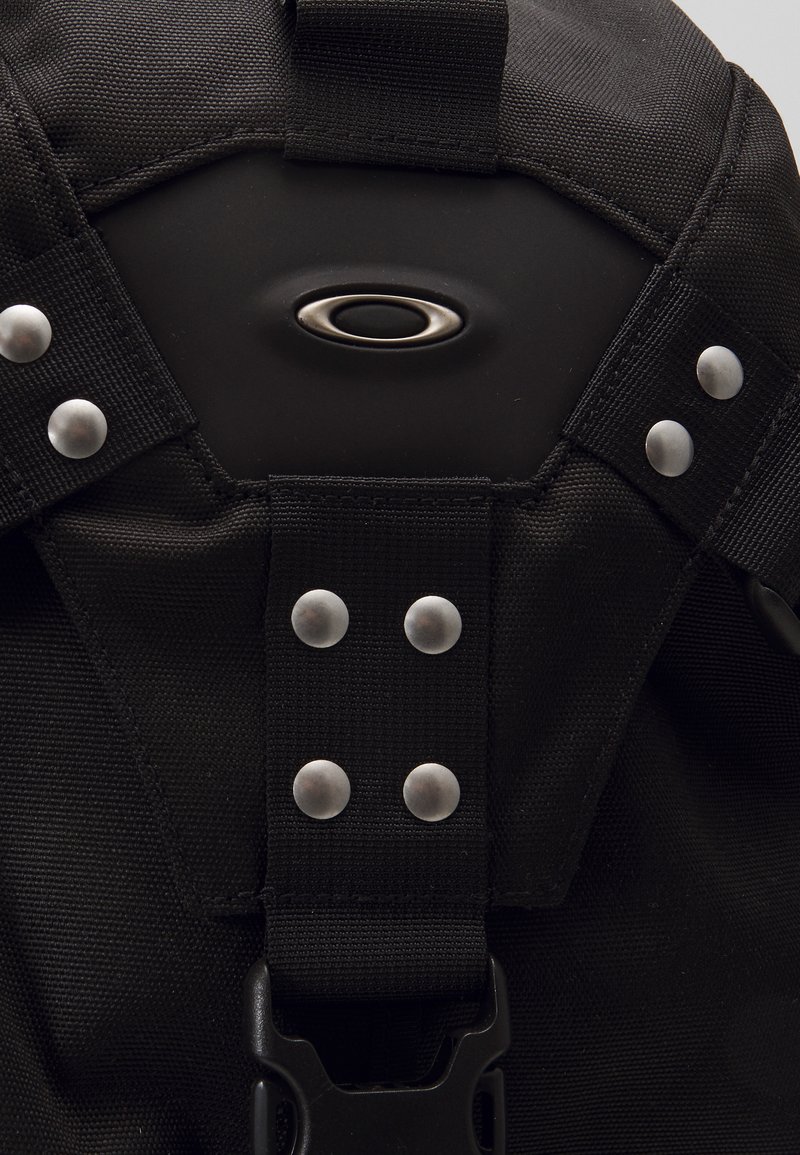 Black backpack featuring silver hardware, reinforced straps, and a central logo. Material has a textured finish and is durable for outdoor use.