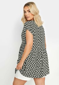 Svart blus med vita prickar, korta ärmar, rundad nederkant och lös passform. Lättviktsmaterial med veckad detalj i ryggen. Vita shorts som matchar.