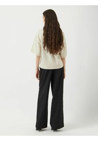 Krémový pletený svetr s širokými krátkými rukávy, zkombinovaný s dobře padnoucími černými kalhotami s širokými nohavicemi, které zdůrazňují uvolněnou siluetu a jemnou texturu.