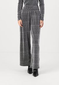 Pantalons à larges jambes en tissu gris texturé avec des fils métalliques. Taille haute avec des plis subtils, associés à des bottines noires.