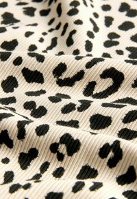 Tessuto con stampa leopardata caratterizzato da macchie nere su una trama a coste beige, che mostra forme e dimensioni variabili nel motivo.