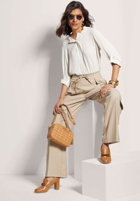 Beige wijde broek in combinatie met een witte overhemd. Bruine hakken loafers, een gewatteerde bruine handtas en ronde zonnebrillen maken de look compleet.