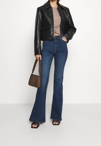 Černá zkrácená kožená bunda, světlý hnědý žebrovaný top, tmavě modré zvonové džíny s vysokým pasem, černé sandály a hnědá kabelka se vzorem.