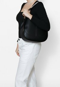 Borsa a spalla in pelle nera con una finitura liscia, forma curva e rifiniture in contrasto. Dotata di un manico singolo e hardware in tonalità oro.