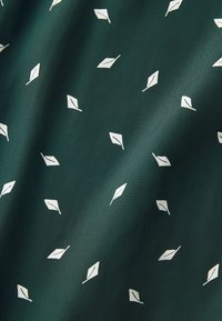 Tissu vert foncé présentant un motif répété de petites feuilles stylisées blanches. La texture semble lisse et légère.