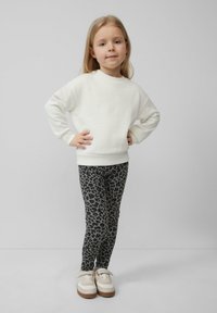 Witte, oversized sweatshirt met geribbelde manchetten en zoom, gecombineerd met zwarte leggings met een grijs luipaardprint. Tan en witte sneakers.