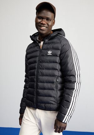 Czarna ocieplana kurtka z zamkiem z przodu, białe paski na rękawach i logo Adidas. Model z kapturem, wykonana z teksturowanego materiału, lekkiego.