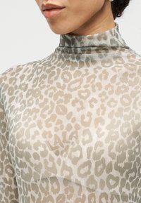 Διαφανές μπλουζάκι σε καφέ απόχρωση με μοτίβο λεοπάρδαλης. Ψεύτικος λαιμός και ελαφριά υφή. Διακριτικό λογότυπο ορατό στο μοτίβο.