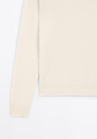 Light beige knit sweater featuring a ribbed cuff, relaxed fit, and a smooth texture. The hem is straight with side slits for added comfort.