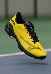 Baskets de sport jaunes avec une tige texturée, des lacets noirs et un accent argenté stylisé. Dispose d'une semelle rembourrée pour un soutien.