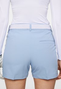 Ljusblå shorts i slätt material, med ett midjeband med fläta och en enkel ficka på baksidan.