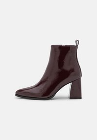 Bordowy lakierowany botek na kostkę z ostrym noskiem, smukłą sylwetką i masywnym obcasem, wyposażony w tylną pętlę ułatwiającą zakładanie.