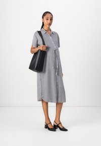 Abito a righe in bianco e nero, con maniche corte, vita con cintura e lunghezza a metà gamba; abbinato a una borsa nera e tacchi.