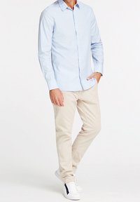 Camicia blu chiaro con maniche lunghe, abbinata a pantaloni beige e sneakers bianche. La camicia ha un colletto tradizionale e una texture liscia.