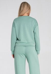 Miętowo zielona, casualowa bluza z okrągłym dekoltem, opadającymi ramionami i ściągaczami na rękawach, w połączeniu z pasującymi spodniami z tego samego materiału.