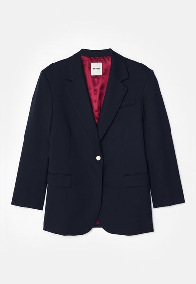 Tumesinine bleiser, millel on istuv disain, ühe hõbedase nööbiga kinnine, kaks esist taskut ja punane satiinvooder. Pehme tekstuur, kohandatud kuju.