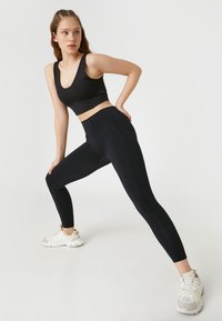 Svart sport-bh och högmidjade leggings i stretchigt tyg. Leggingsen har sidopaneler och en slät yta, tillsammans med vita träningsskor.