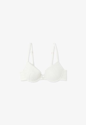 White lace bra with molded cups, adjustable straps, and a decorative gold-tone hardware detail at the center front. Textured floral pattern.