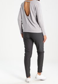 Szara bluzka z długim rękawem z wycięciem z tyłu, zestawiona z ciemnymi spodniami w prążki, do tego białe trampki. Miękka faktura, casualowy design.