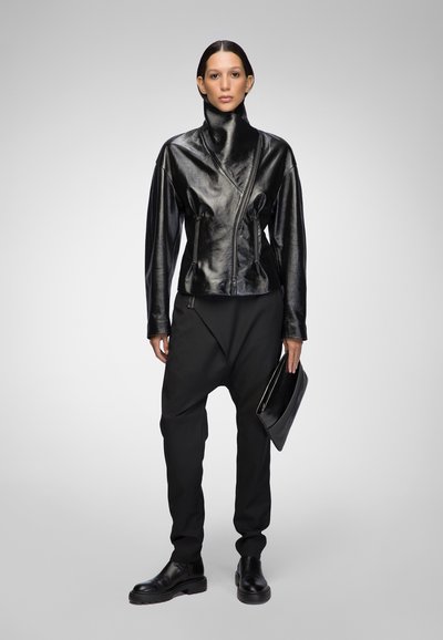 Black leather jacket with high collar and asymmetrical front zip, paired with relaxed-fit black pants and black clutch. Smooth texture.