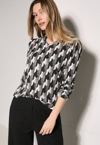 Mustat ja valkoiset kuviot, V-pääntie ja pitkät hihnat, houndstooth-kuvio. Pehmeä kangas rentoa istuvuutta varten.