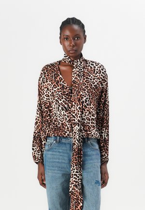 Leopard-print, silky blouse with long sleeves and a neck tie, featuring shades of brown and cream, worn with blue denim jeans.