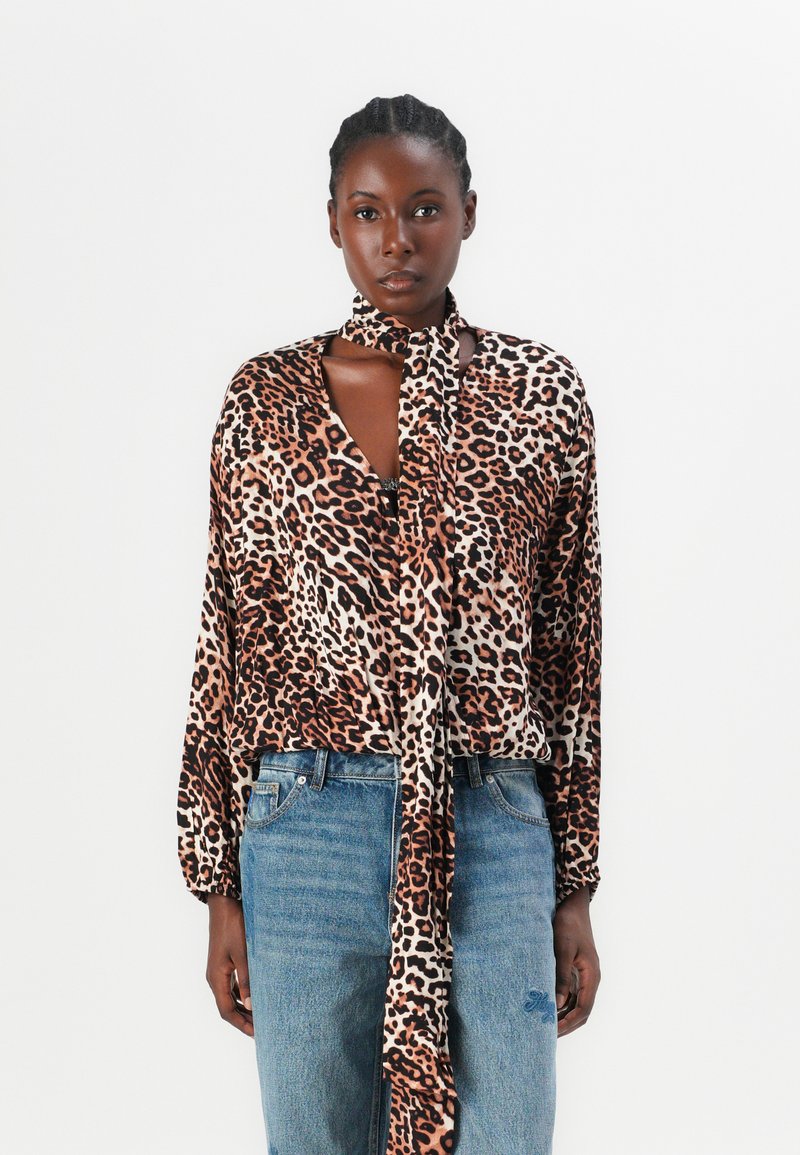 Leopardenmuster, seidige Bluse mit langen Ärmeln und einem Halstuch, in Braun- und Cremetönen, getragen mit blauen Denim-Jeans.