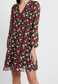 Svart blommig klänning med långa, puffiga ärmar, en V-ringning och en volangkjol. Tyget har röda och vita blommönster.